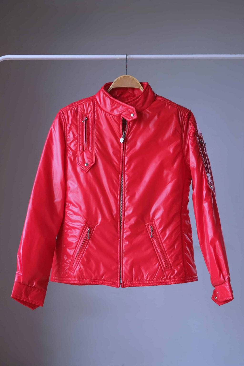 Full front view of a vibrant red vintage 1970s Mossant technical ski jacket on a wooden hanger. It features a quilted nylon shell, an asymmetrical snap collar, two slanted waist pockets, and a vertical chest pocket.