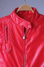 Close-up of the upper chest and collar of the red Mossant jacket. Details show the padded stand-up collar with a snap-button flap, the silver-tone crest zipper pull, and the vertical zippered chest pocket with a decorative pointed leather-style trim at the bottom.