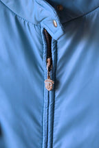 A tight macro shot of the sky blue Mossant ski jacket’s central zipper. The silver-tone zipper pull is embossed with the Mossant brand crest, featuring a winged horse (Pegasus) design.