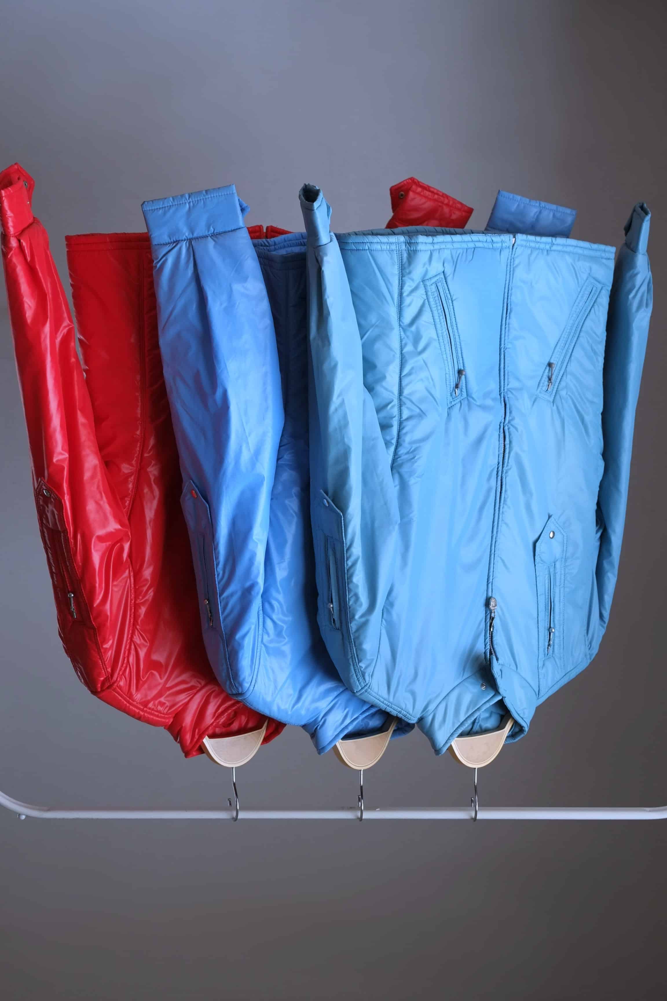 Three vintage Mossant technical ski jackets hanging in a row on a clothing rack, showcasing the available colorways: sky blue, steel blue, and bright red. The shot emphasizes the consistent "Natacha" model design across different colors.