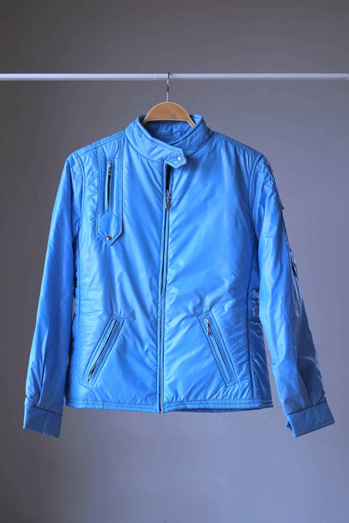 Full front view of the sky blue Mossant vintage 70s ski jacket on a wooden hanger. The jacket features a slim, athletic fit, technical zippered pockets on the chest and waist, and a snap-closure high collar.