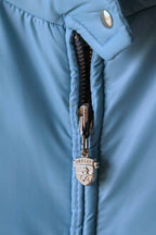 A tight macro shot of the steel blue Mossant ski jacket’s central zipper. The silver-tone zipper pull is embossed with the Mossant brand crest, featuring a winged horse (Pegasus) design.
