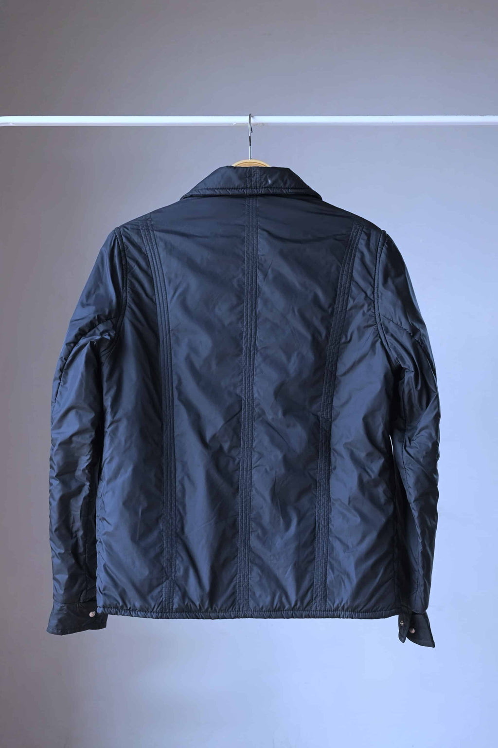 Rear view of the black quilted ski jacket on a hanger, highlighting the vertical stitched panels and clean, tailored construction.