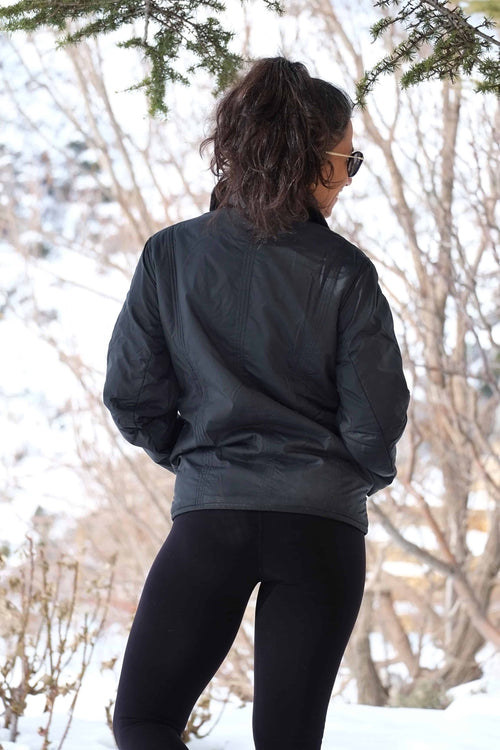 A rear view of the woman wearing the Mossant jacket in the snow, showcasing the vertical quilting and how the jacket sits at the waist.