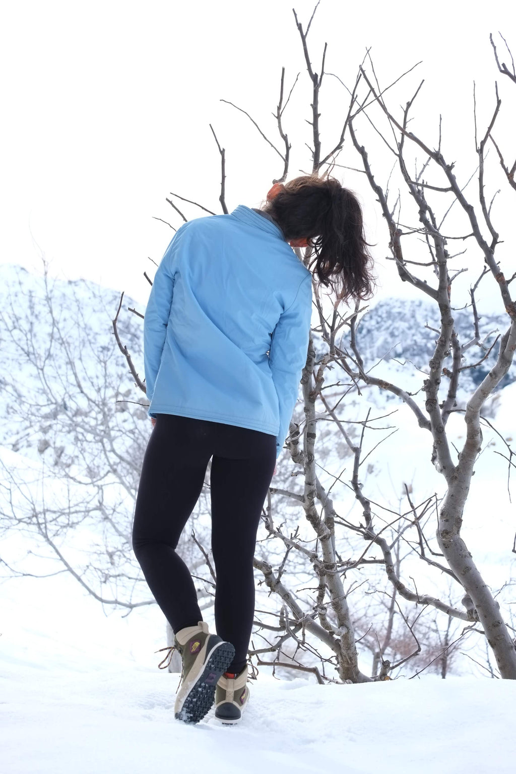 Rear view of a model wearing a light blue vintage Mossant ski jacket in a snowy mountain setting, showing the clean back construction and mandarin collar.