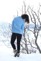 Rear view of a model wearing a light blue vintage Mossant ski jacket in a snowy mountain setting, showing the clean back construction and mandarin collar.