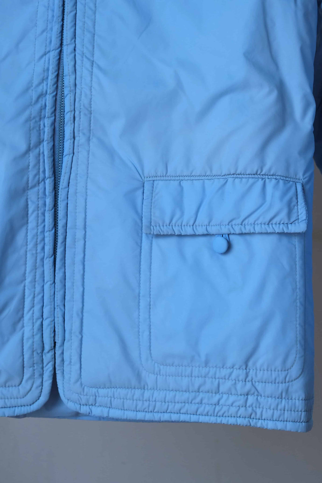 Detail shot of the jacket’s front square flap pocket, featuring tonal blue stitching and a decorative fabric-covered button.