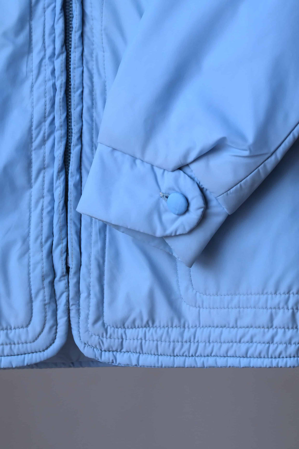 Close-up of the jacket's lower hem and sleeve cuff, showing the multi-row horizontal topstitching and a button-closure cuff detail.