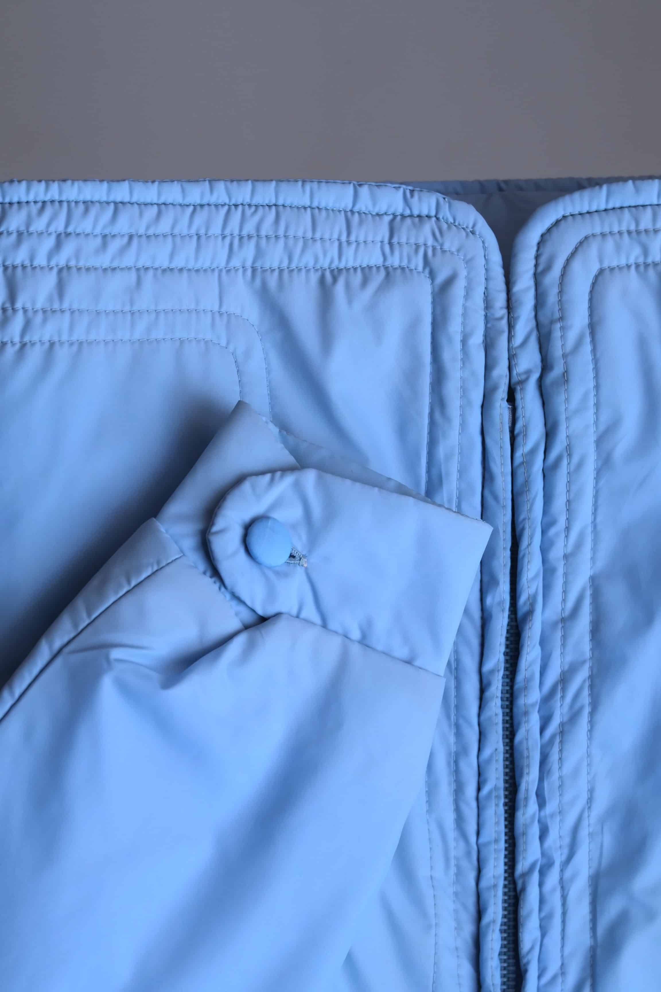 Close-up of the jacket's lower hem and sleeve cuff, showing the multi-row horizontal topstitching and a button-closure cuff detail.