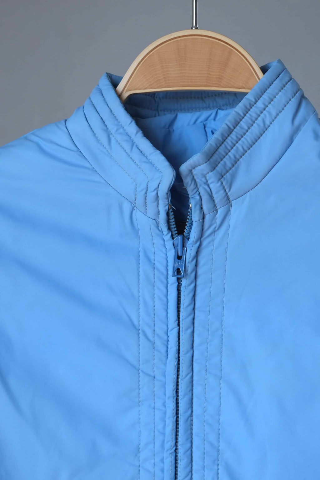 A focused shot of the upper portion of the jacket, highlighting the ribbed mandarin collar and the color-matched blue zipper hardware.