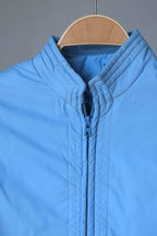 A focused shot of the upper portion of the jacket, highlighting the ribbed mandarin collar and the color-matched blue zipper hardware.