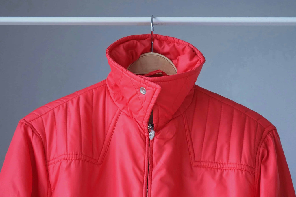 Detailed shot of the jacket with the collar zipped up and snapped into a tall standing position, highlighting the horizontal quilting on the neck.