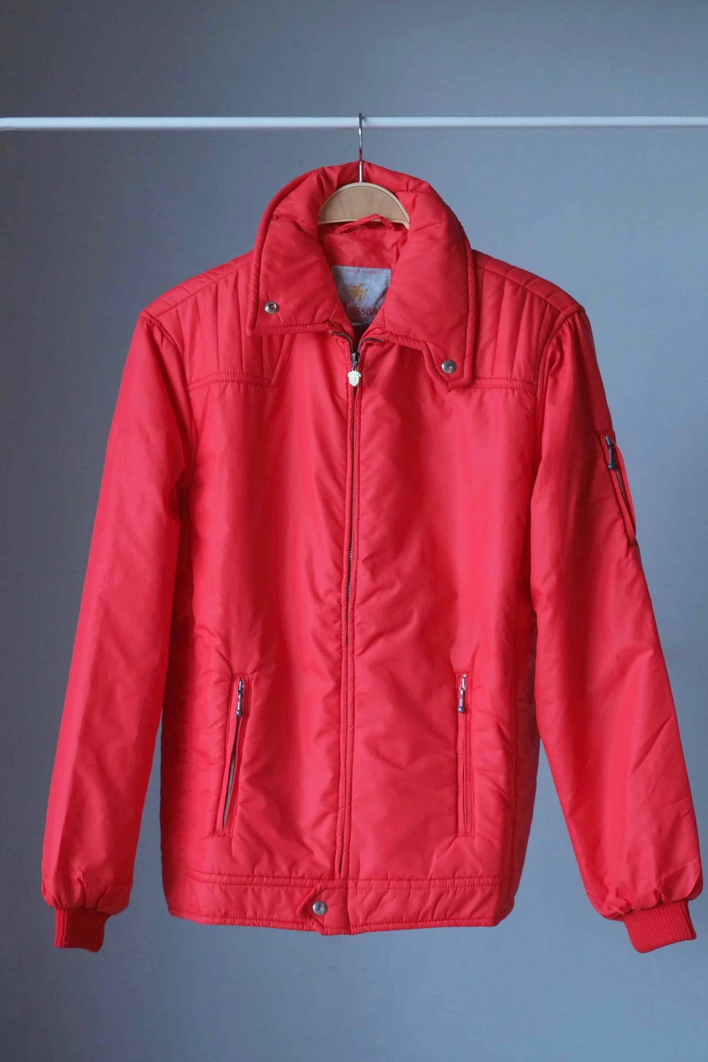 Full front view of a red vintage 70s Mossant matte-finish padded ski jacket on a wooden hanger, featuring vertical quilted shoulder panels and a wide-spread collar.