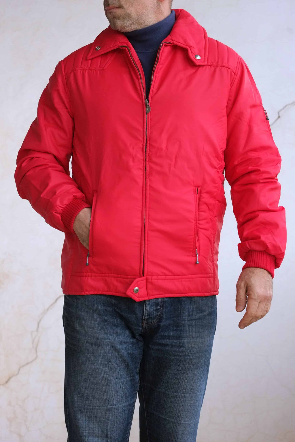 A man wearing the red matte Mossant jacket with one hand in the zippered pocket, styled with a dark turtleneck and blue jeans.