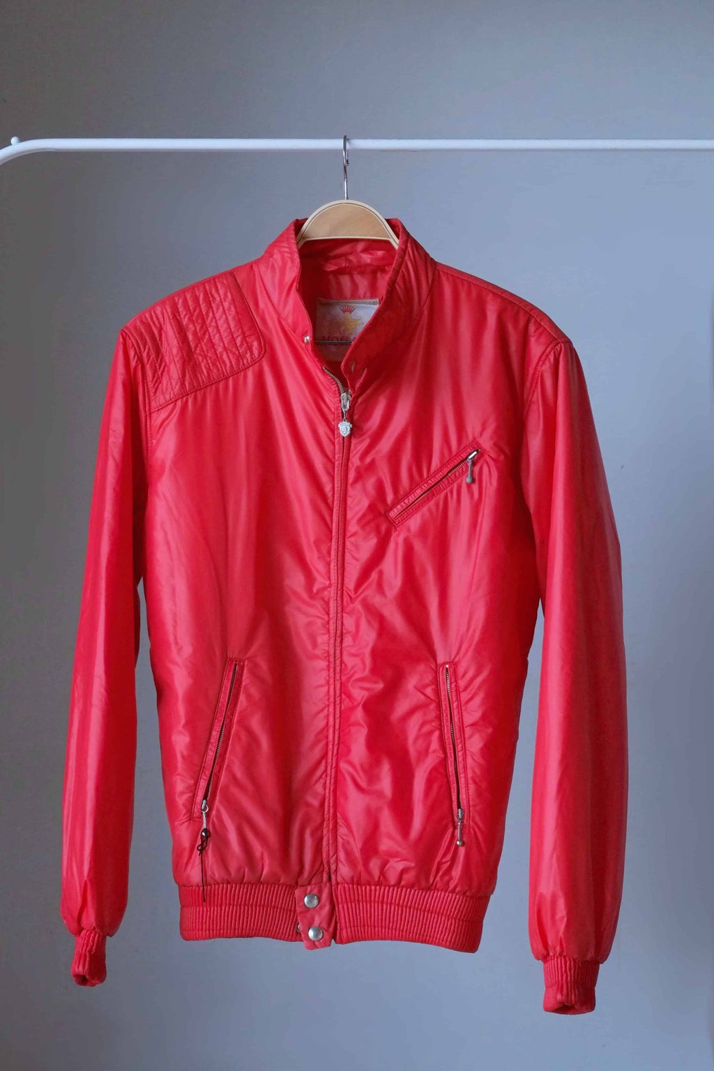 Front full-length view of a bright red vintage 70s Mossant lightweight puffer ski jacket hanging on a white rack, featuring a ribbed waistband and cuffs.