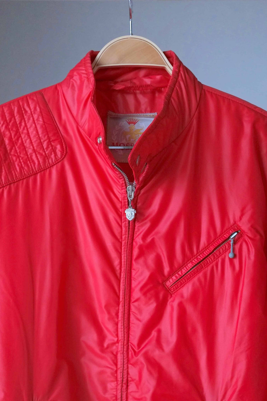 Close-up of the upper half of the red Mossant jacket, showing the quilted shoulder padding, stand-up collar, and a diagonal zippered chest pocket.