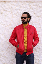 A male model wearing the red 70s puffer jacket over a yellow turtleneck and jeans, demonstrating the fit and vibrant color against a stone wall background.