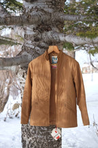 A vintage MOSSANT 70s camel brown quilted ski jacket hanging on a wooden hanger against a snowy outdoor background.