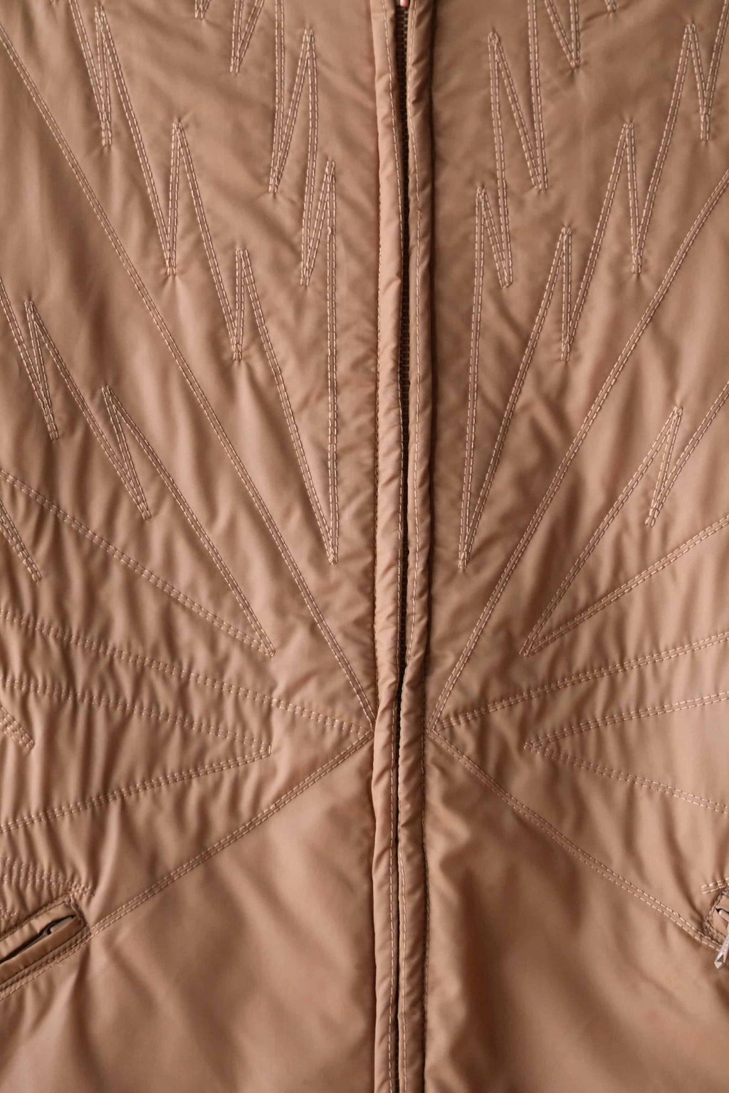 Detailed view of the unique decorative "lightning bolt" zigzag stitching on the front of the camel brown Mossant jacket.