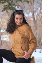 A woman smiling while wearing the belted Mossant camel brown ski jacket in a snowy outdoor setting.