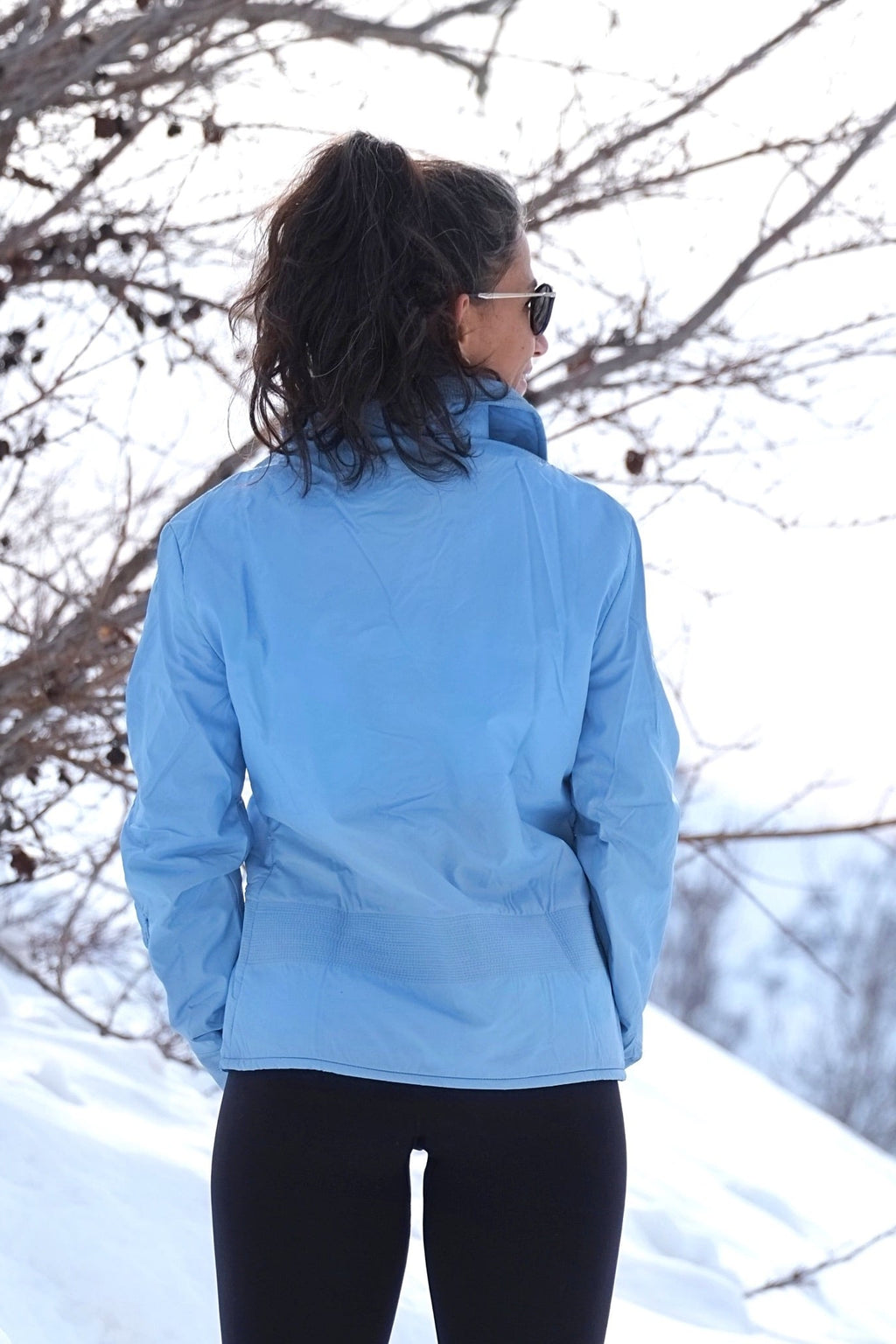 A woman outdoors in a snowy setting wearing the sky-blue vintage ski jacket, viewed from the back to highlight the waist ribbing and structured fit.
