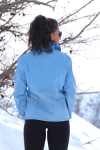 A woman outdoors in a snowy setting wearing the sky-blue vintage ski jacket, viewed from the back to highlight the waist ribbing and structured fit.