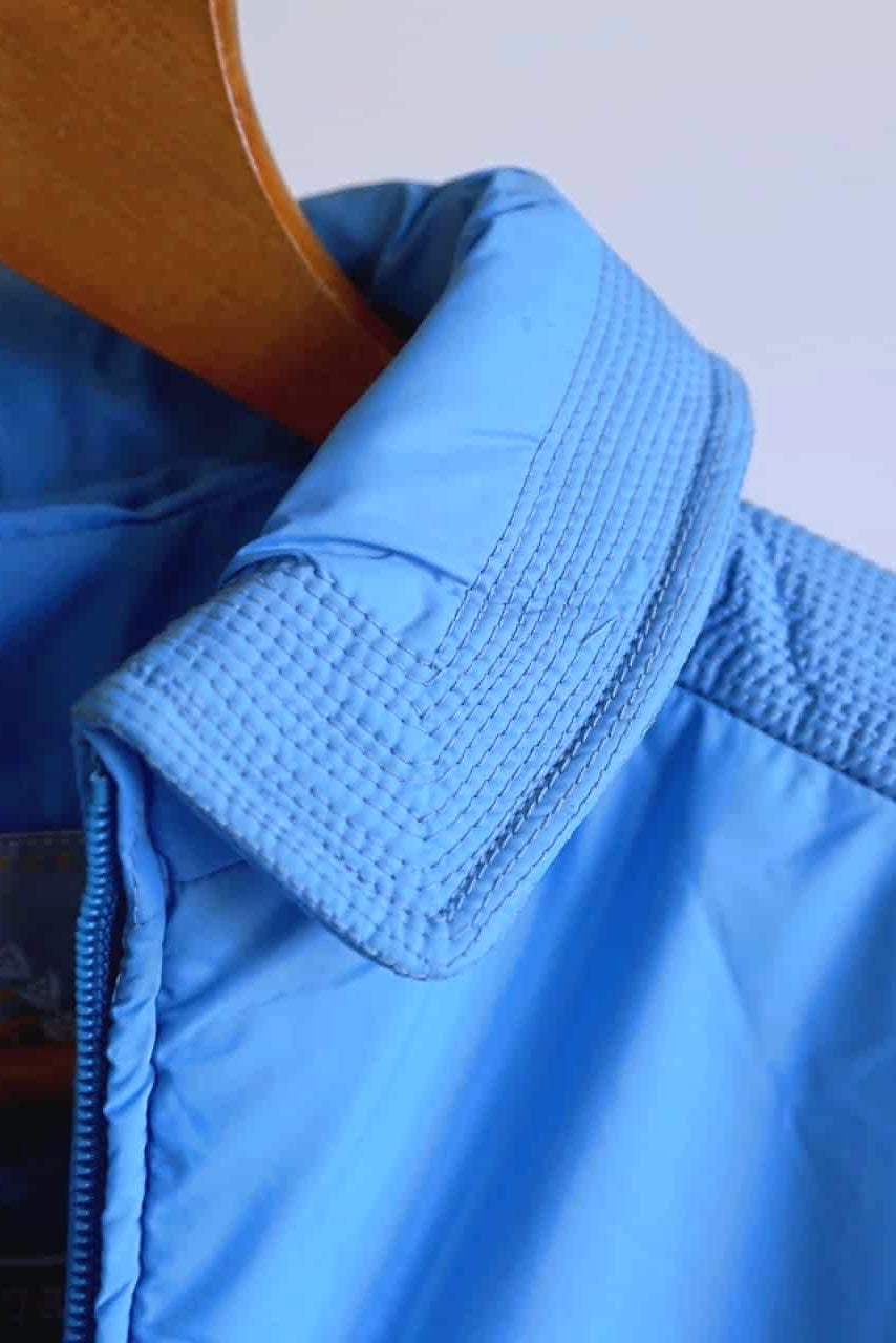 A close-up of the sky-blue jacket’s pointed collar, showcasing the intricate multi-row decorative stitching and textured finish.