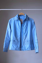 A front view of the 1970s sky-blue Mossant Aral ski jacket, unzipped to reveal the vintage Paris neck label, featuring horizontal zip pockets and smocked waist detailing.