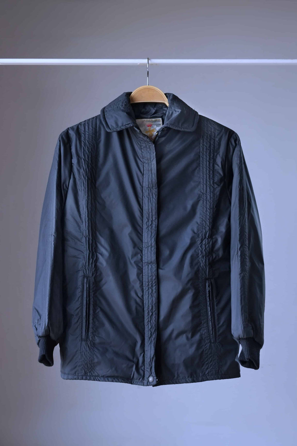 Front view of a vintage 70s Mossant black straight-cut ski jacket featuring vertical quilted detailing and a classic collar on a hanger.