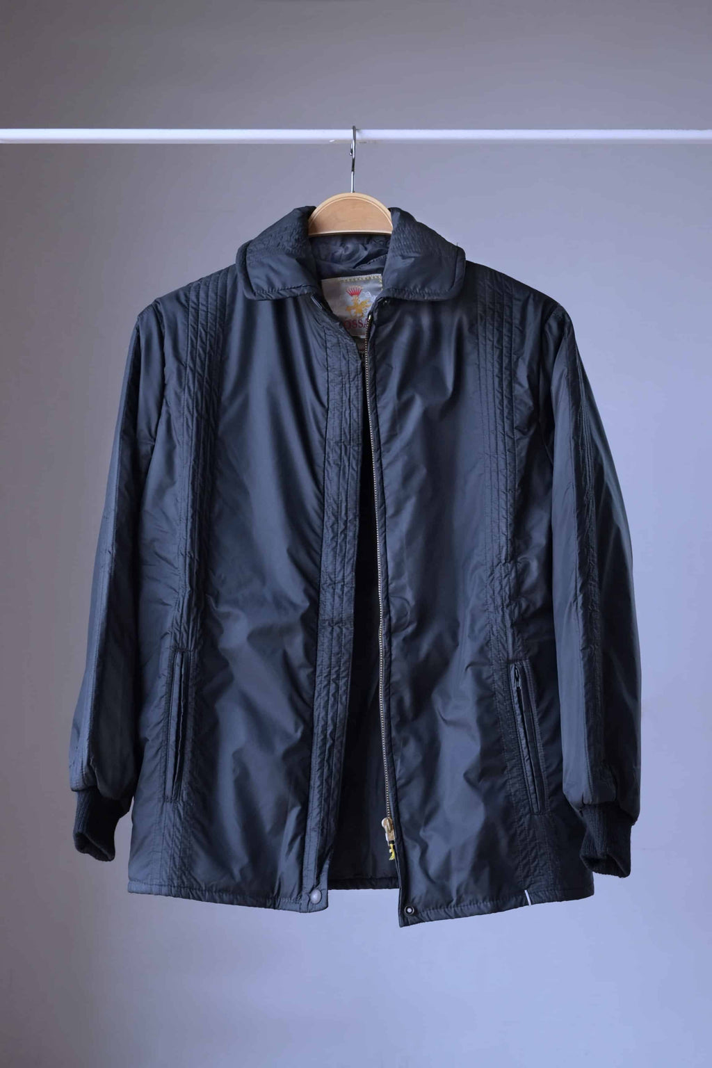 Studio shot of a black vintage Mossant 1970s ski jacket with an open zipper, showing the interior lining and ribbed knit cuffs.