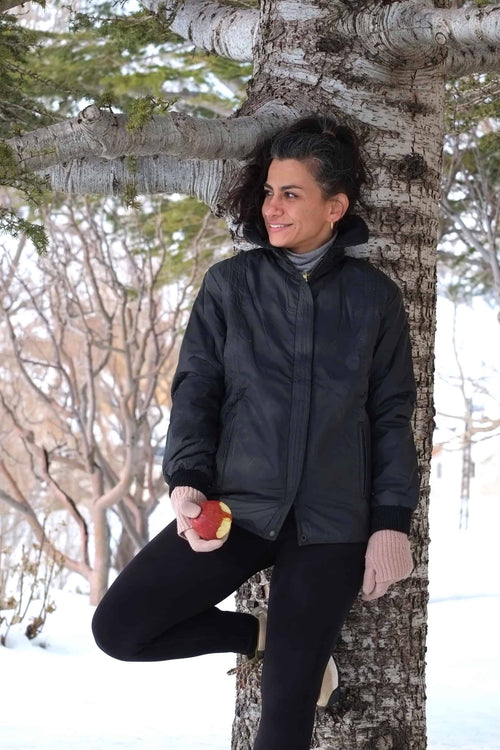 Female model wearing the Mossant vintage black straight-cut ski jacket in the snow, styled with beige gloves and a grey turtleneck.