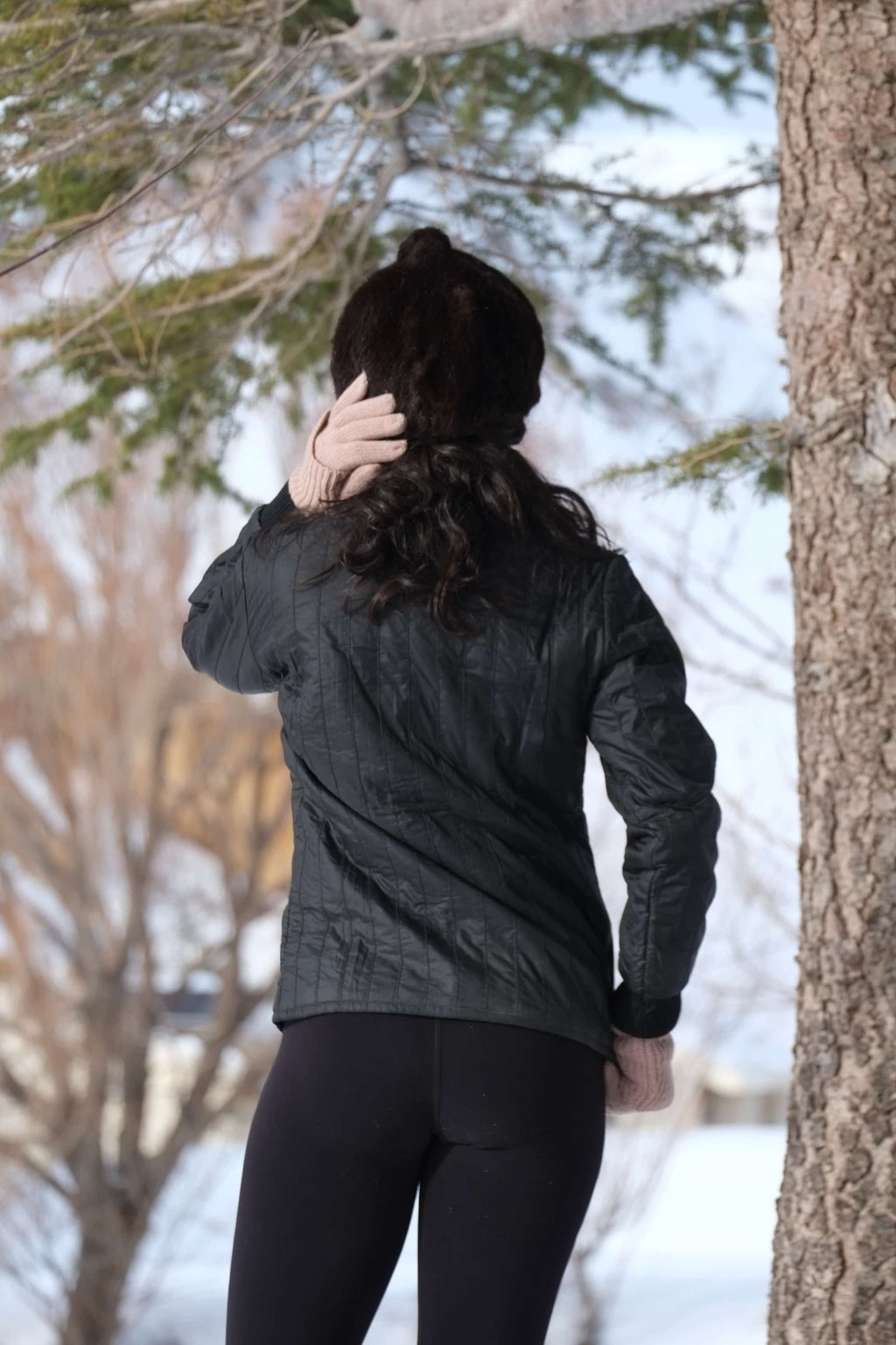 Rear view of a person wearing a black vintage 1970s Mossant ski jacket in a snowy outdoor setting. The jacket features distinct vertical quilting, a slim fit, and ribbed black cuffs.