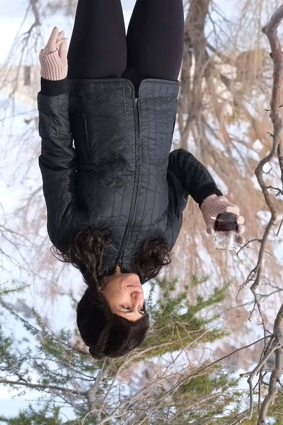 A person outdoors in the snow wearing a black 1970s Mossant quilted ski jacket, styled with a dark faux fur hat and pink knit gloves. The vertical stitching and lightweight puffer design are clearly visible.