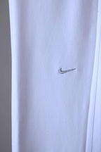 Close-up of a silver Nike swoosh logo embroidered on the right hip of white pants.