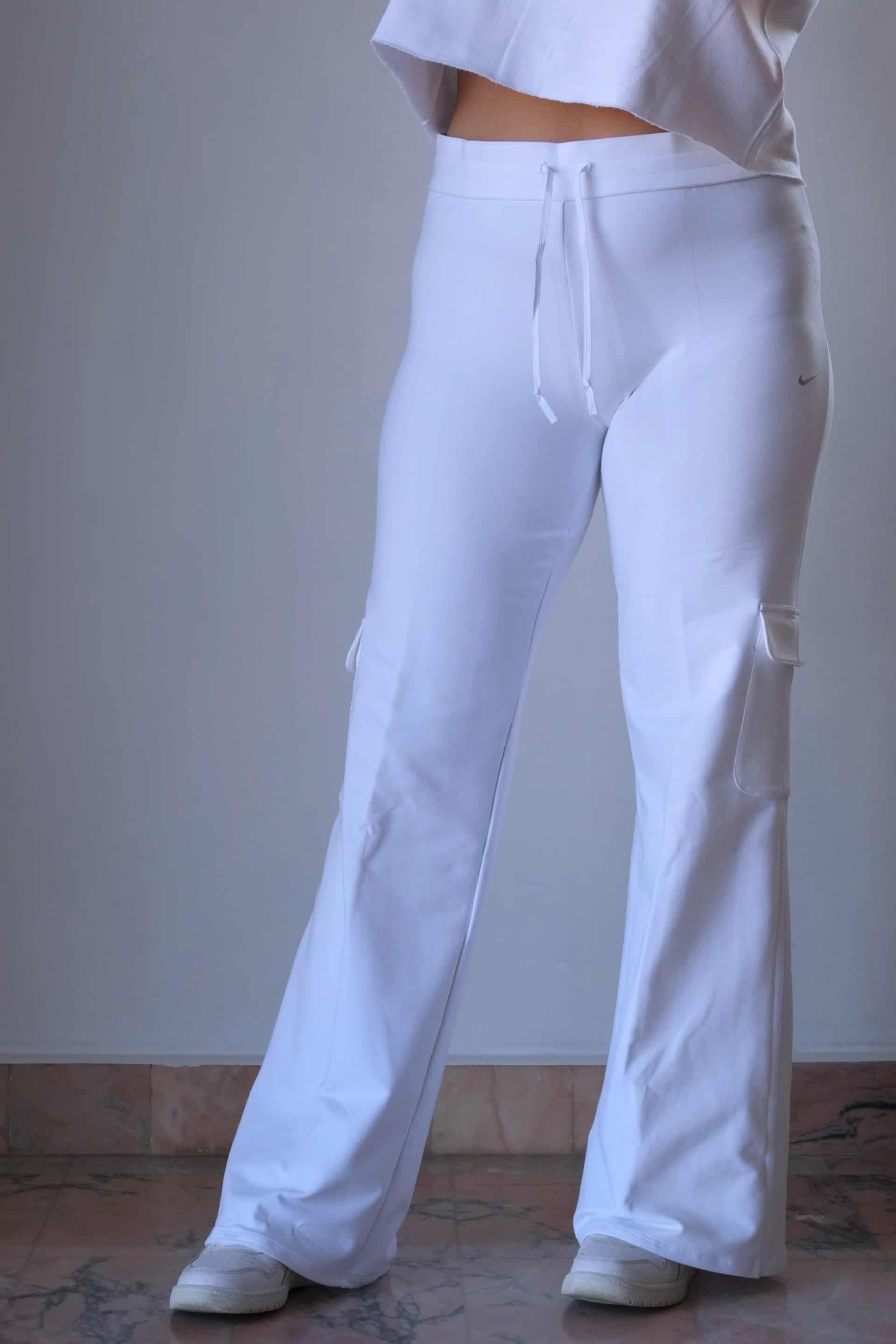 A model wearing white Nike flared pants from the 2000s era, featuring a drawstring waist and subtle cargo pockets, standing indoors on a marble floor.