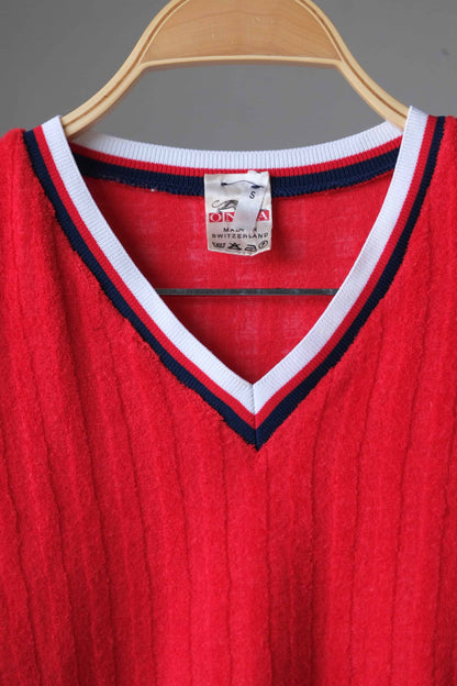 Close-up showing the ONZA brand tag, size S, and the white and navy striped V-neck of a red vintage sweater. The tag indicates "Made in Switzerland.