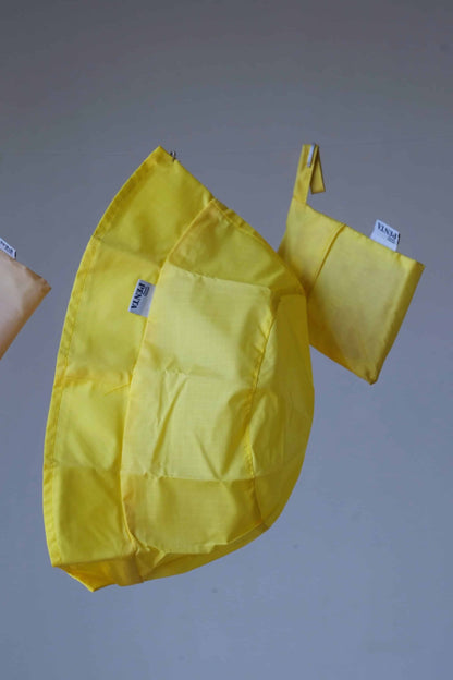Yellow rainproof bucket hat with its pouch hanging in front of a grey background