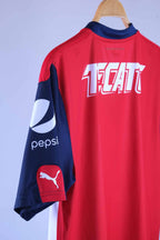 Close-up view of the back shoulder and navy blue sleeve, detailing the white "TECATE" graphic text across the upper back, a white "pepsi" logo printed on the side of the sleeve, and a red patch with a white Puma logo near the cuff.