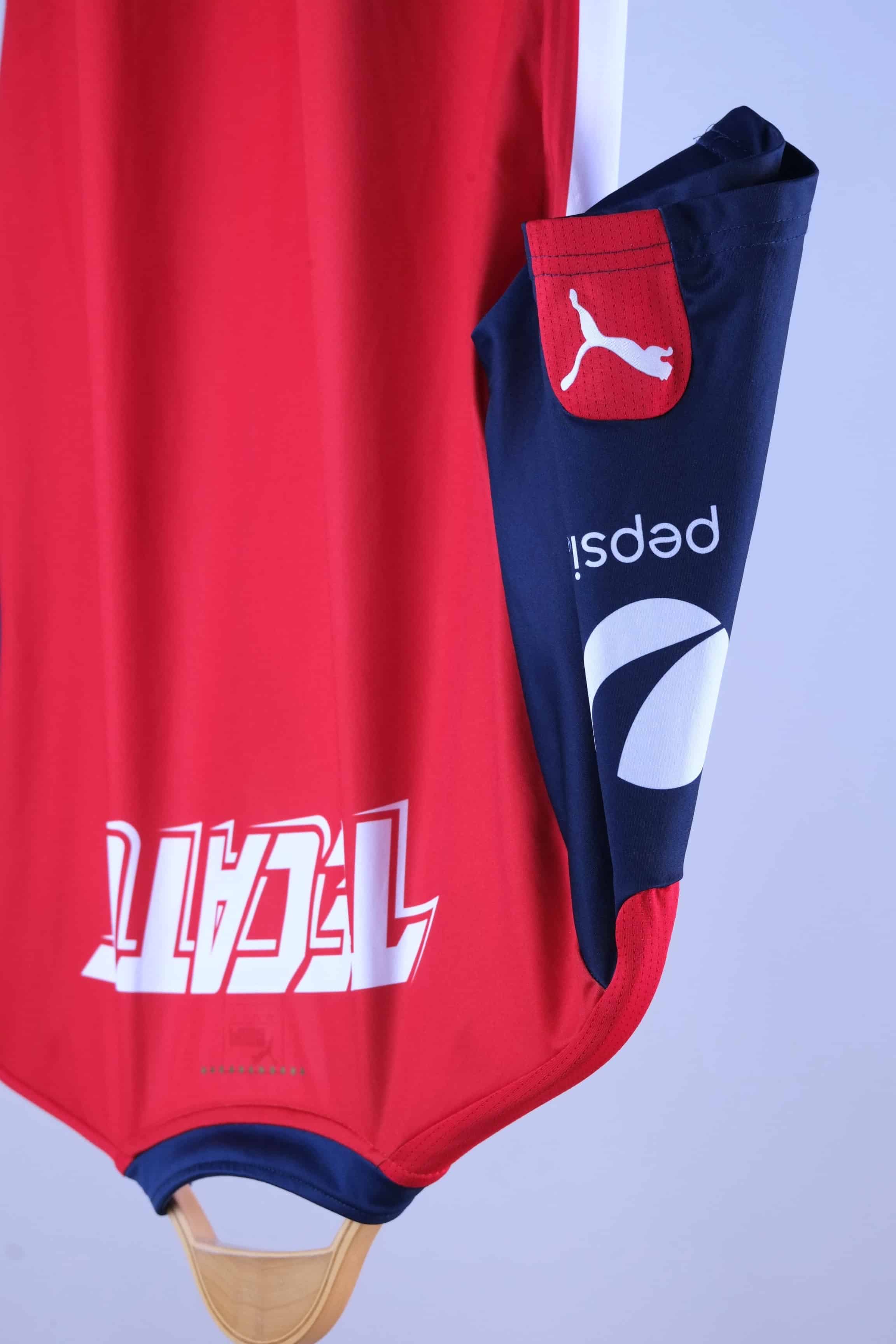 Close-up view of the back shoulder and navy blue sleeve, detailing the white "TECATE" graphic text across the upper back, a white "pepsi" logo printed on the side of the sleeve, and a red patch with a white Puma logo near the cuff.