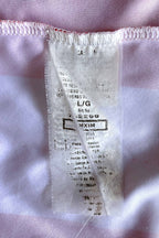 Close-up of a long, semi-translucent white fabric care label stitched inside the shirt against a red and white striped backdrop. The tag displays printing that includes the sizing "L/G", "Art No. 762299", "MXIM", and manufacturing details indicating it was made in Mexico.