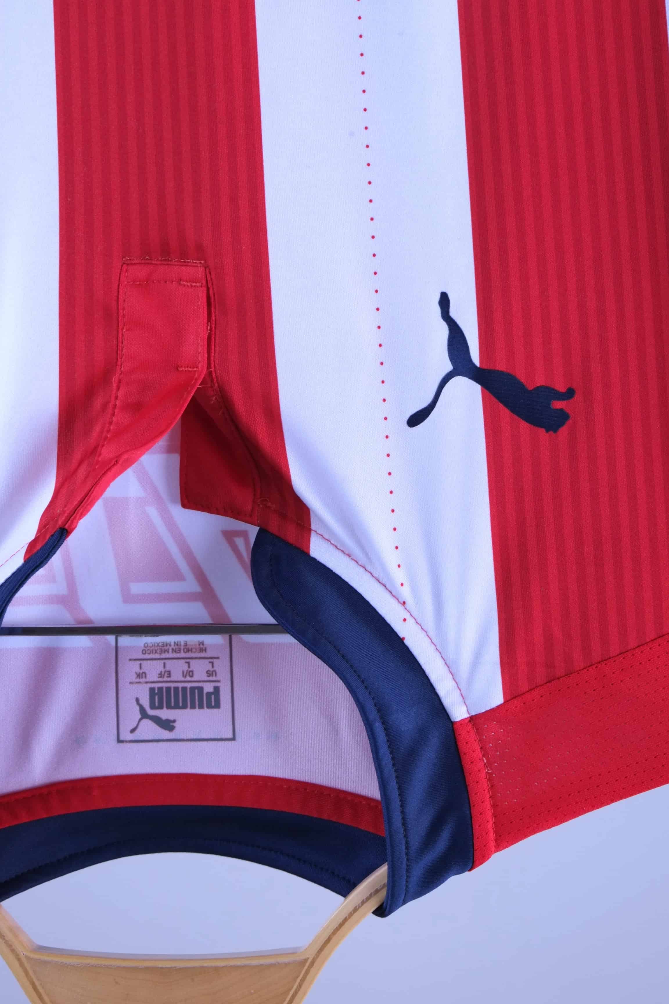Close-up of the jersey's collar area, showing the navy blue buttonless placket, the navy blue embroidered Puma cat logo on the front, and the printed Puma branding/sizing information inside the neckline.