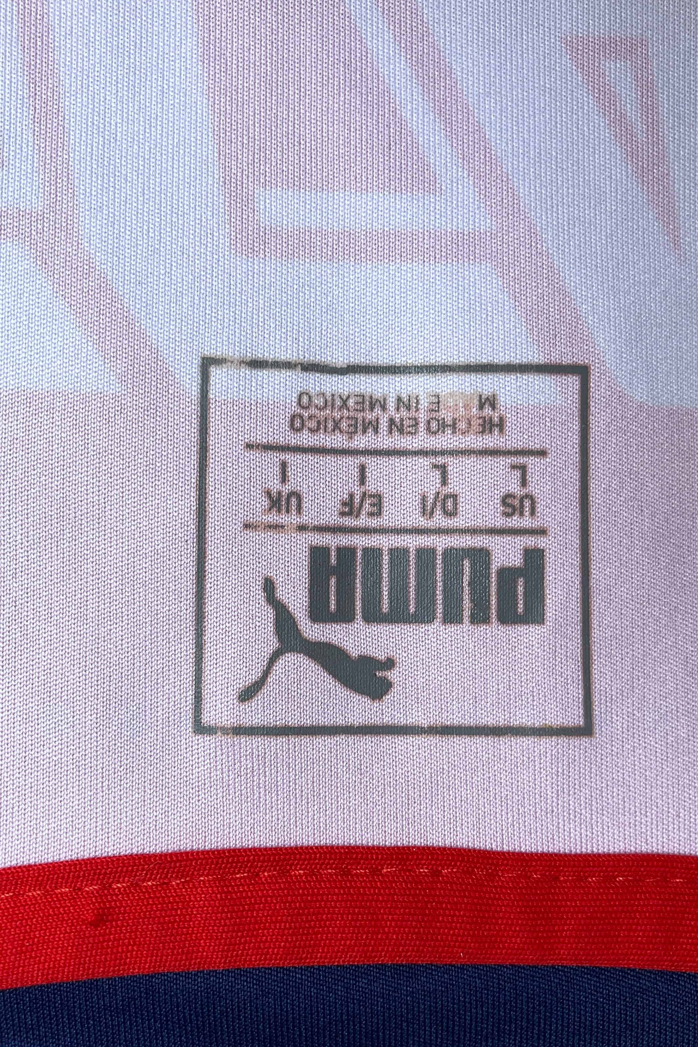 Close-up of the square, heat-pressed size label located on the inner neck. It features the classic Puma logo, text reading "US L / D/I L / E/F L / UK L", and "HECHO EN MEXICO / MADE IN MEXICO" stamped below the sizing grid against the white jersey fabric.