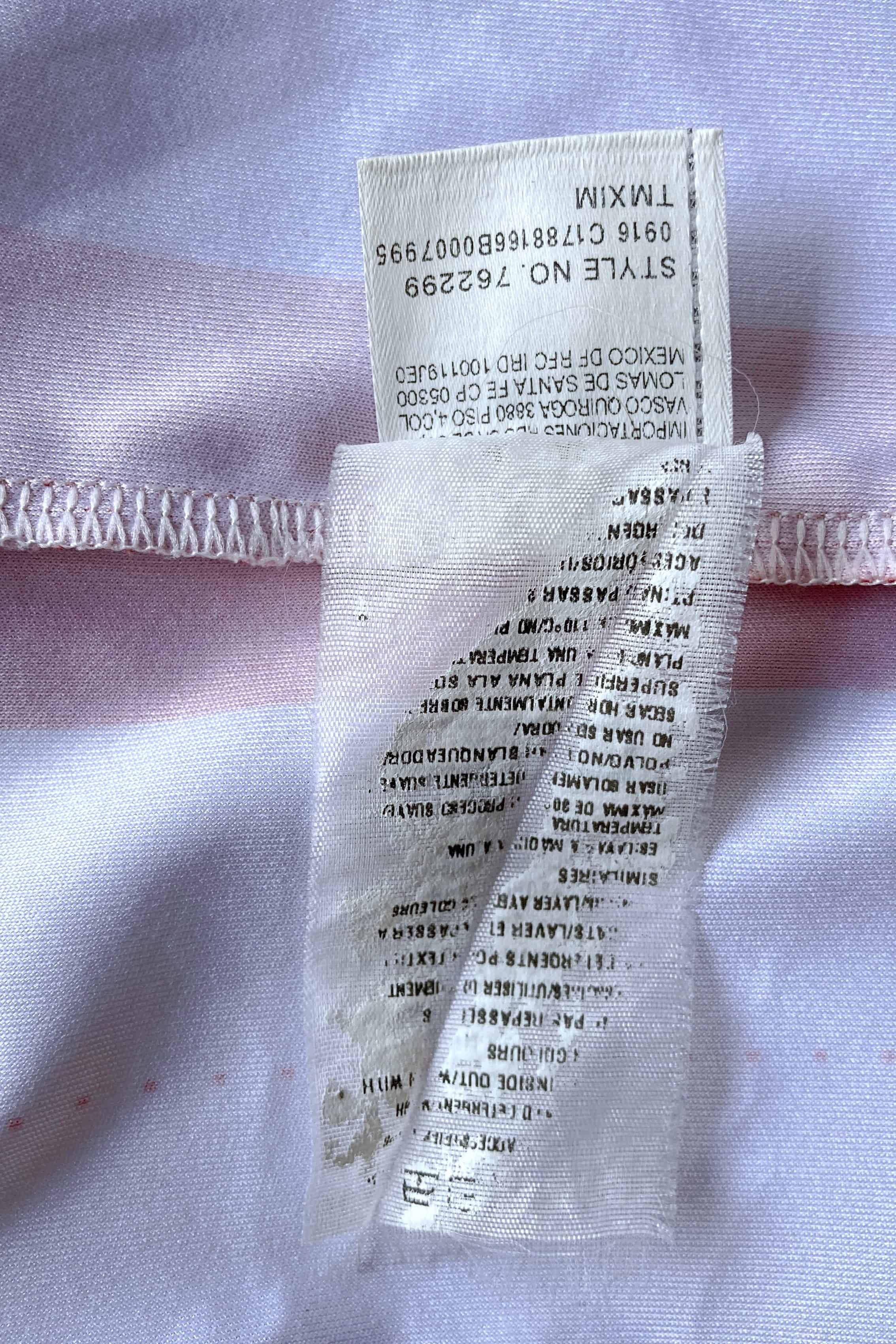 Close-up of the interior washing instructions tag, showing printed text in multiple languages and an attached lower label clearly listing "STYLE NO. 762299", the factory production code "0916 C1788166B0007995", and "TMXIM".