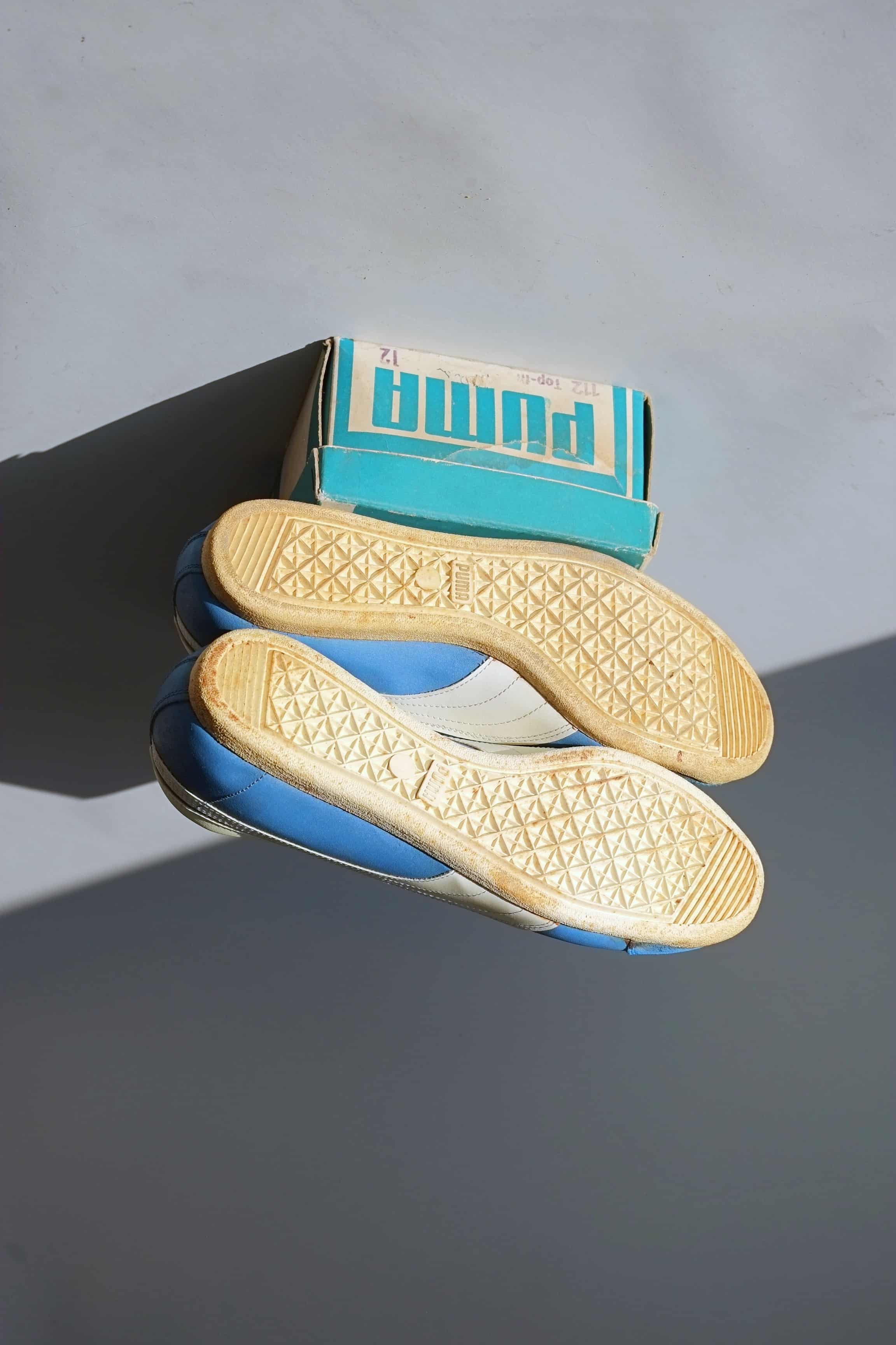 Underside view of intact yellow crepe rubber soles stacked on original teal Puma Dassler box showing model 112 Top-fit size 12 label.