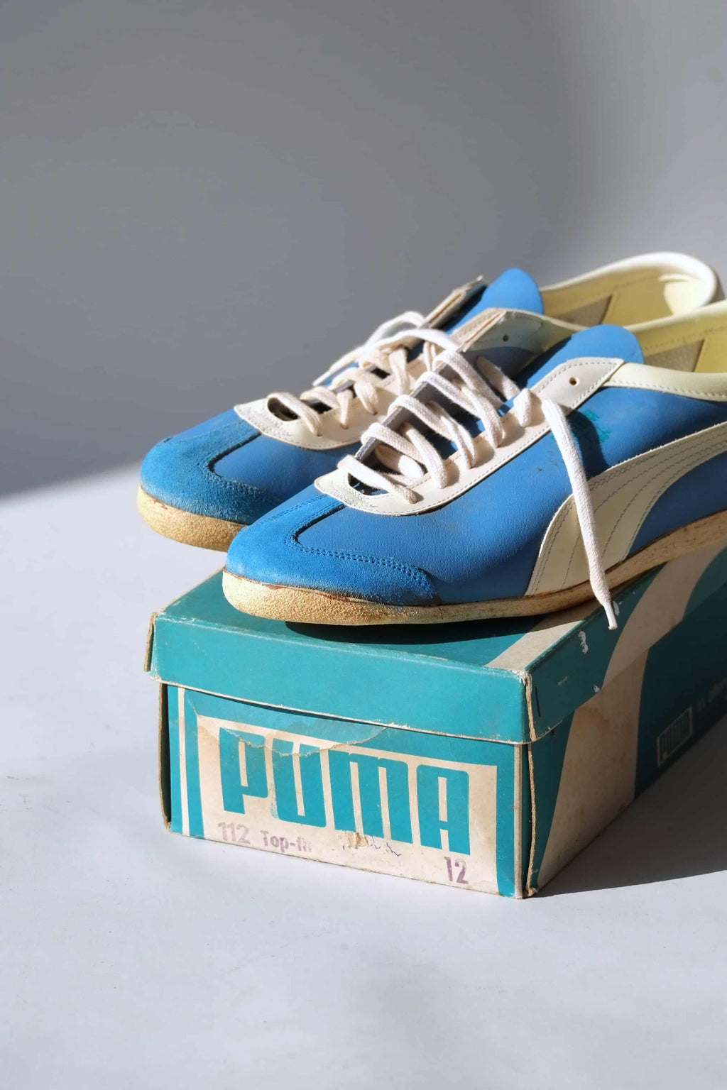 Tight eye-level view of blue leather 1970s Puma Top Fit trainers sitting on original box showing off-white lacing and suede toes.