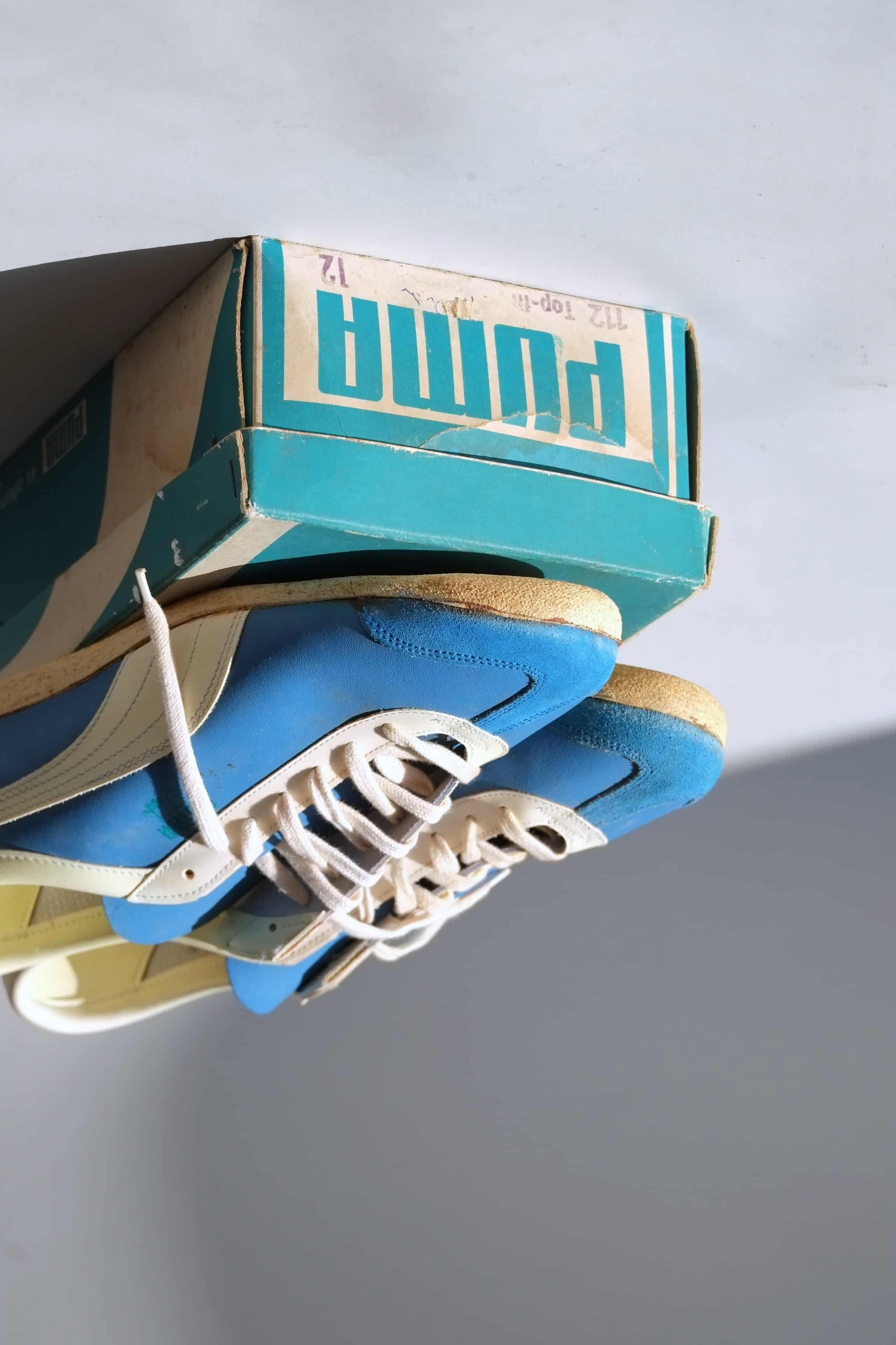 Tight eye-level view of blue leather 1970s Puma Top Fit trainers sitting on original box showing off-white lacing and suede toes.