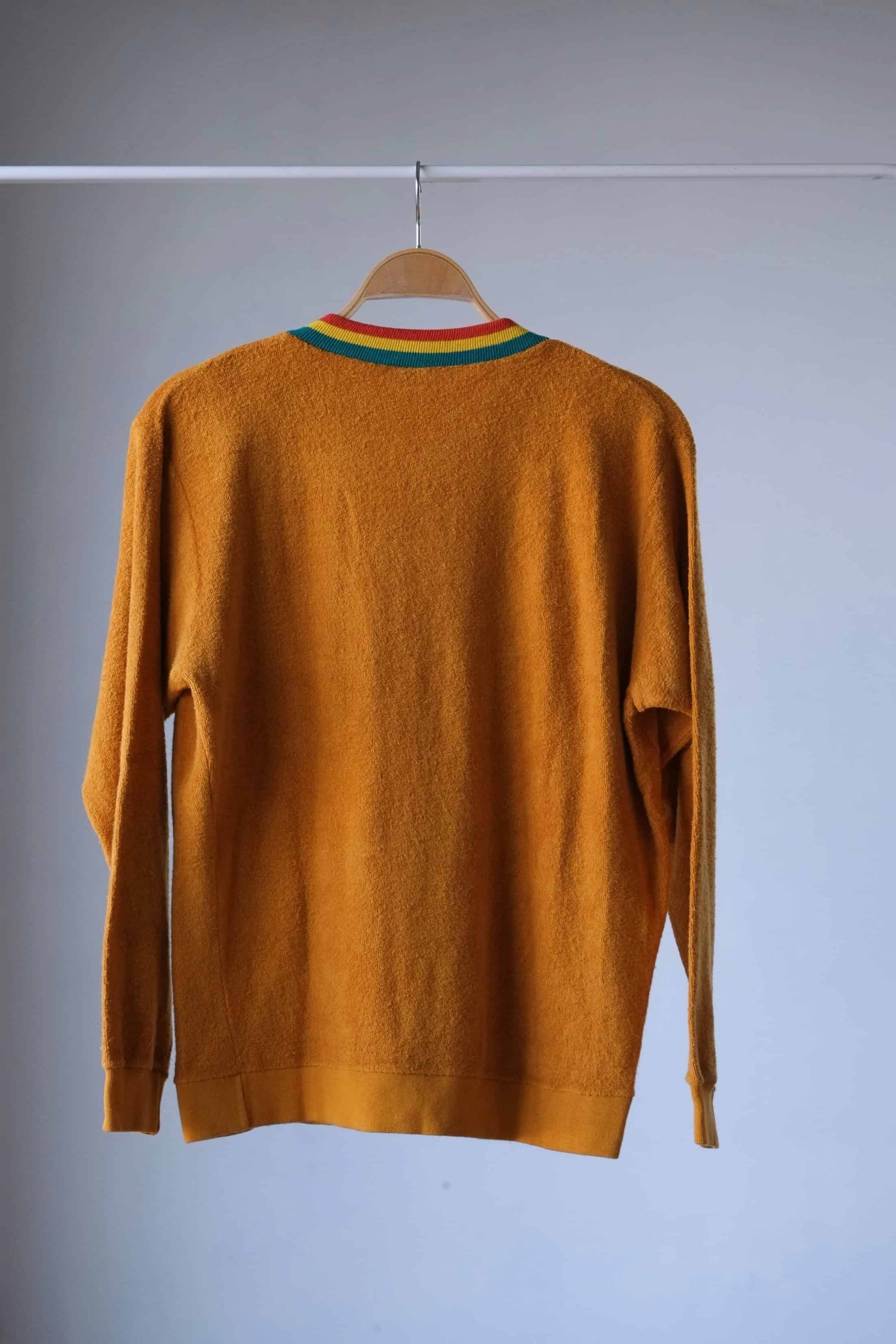 Back view of a Vintage 70s Mustard Terrycloth Sweater with Colorful Striped Neckline displayed on a hanger against a grey background.