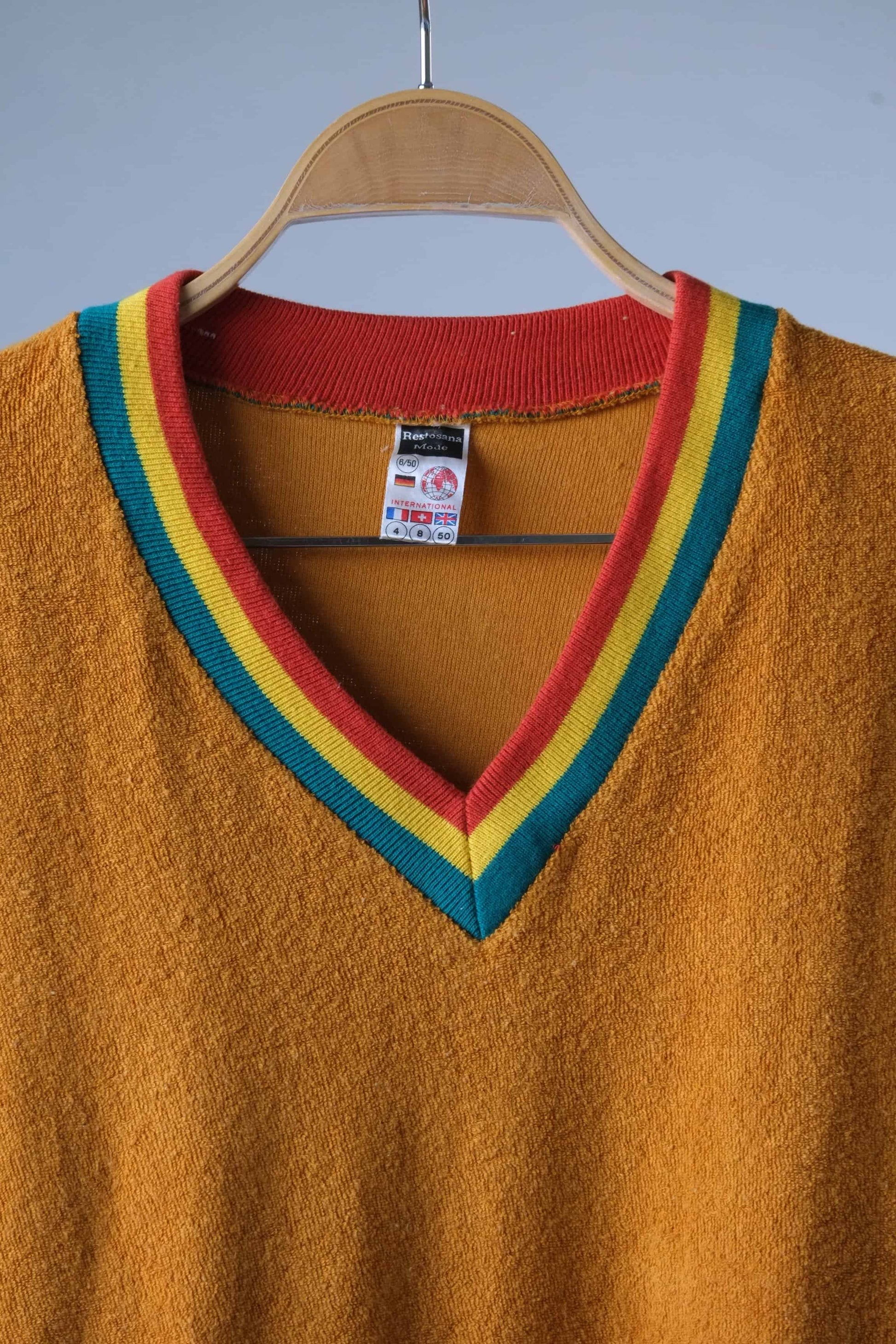 Close shot of a Restosana Vintage 70s Mustard Terrycloth Sweater with Colorful Striped V-Neckline displayed on a hanger against a grey background.