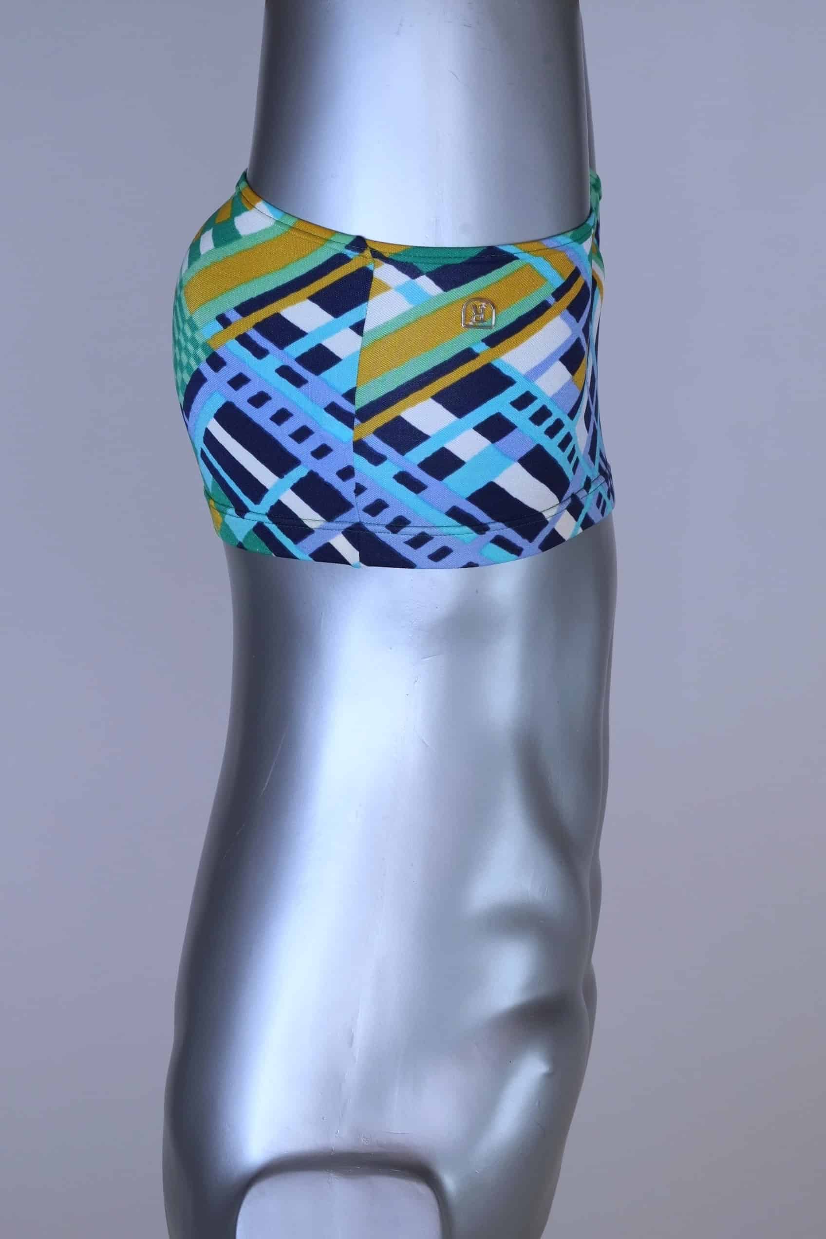 Side view of vintage 70s Ribana swim trunks in a geometric print with cool tones of blue, green, yellow, and navy, modeled on a silver mannequin.
