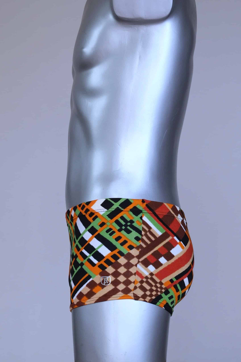 Side view of vintage 70s Ribana swim trunks in a geometric print with warm tones of orange, brown, green, and black, modeled on a silver mannequin.